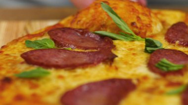 Ahşap bir masanın üzerinde taze taze, iştah açıcı peperoni pizza. Arka planda erkek ya da kadın şefin bulanık figürünün yeşillikleriyle dekore edilmiş. Ön manzara 4K video.