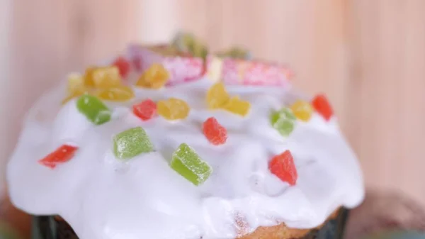 a traditional Easter cake glazed and decorated with marmalade and candied fruits is rotating with colored easter eggs in beautiful glass plate on wooden background in slow motion close-up 4K video