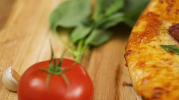 Pizza peperoni appétissante chaude fraîche couchée sur une assiette en bois sur la table décorée de basilic vert, tomate et ail au ralenti close up front view Vidéo 4K — Photo