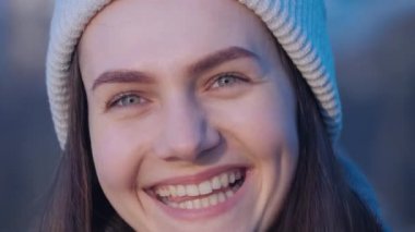 Genç ve güzel yeşil gözlü esmer bir kızın portresi. Başını çevirip kameraya bakıyor ve mutlu bir şekilde gülüyor. Sonra da şehir parkındaki gölün arka planına bakıyor.