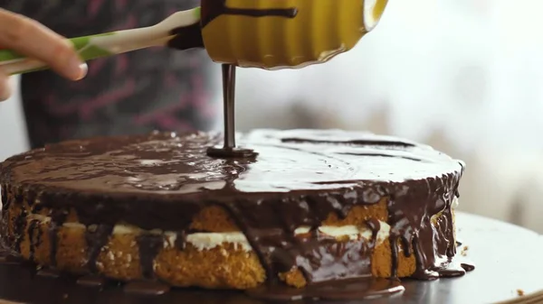 Weibliche Hand gießt die Schokoladencreme auf den Kuchen und beginnt, sich zu verteilen. — Stockfoto