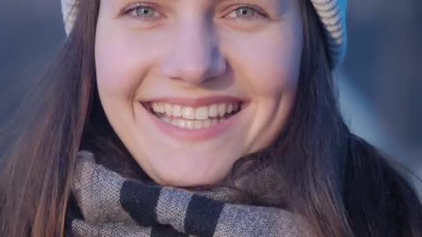 Young beautiful green eyed woman portrait who is correcting her hair and knitted hat, looks at the camera and laughs with a lake in the city center on background in close up 4K video. — 비디오