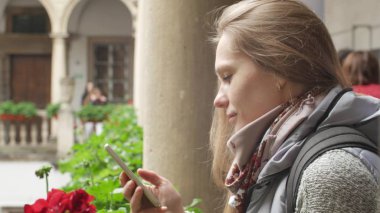 Balkondaki çekici beyaz kız balkonda cep telefonu kullanıyor. Arka planda güzel ortaçağ sütunları