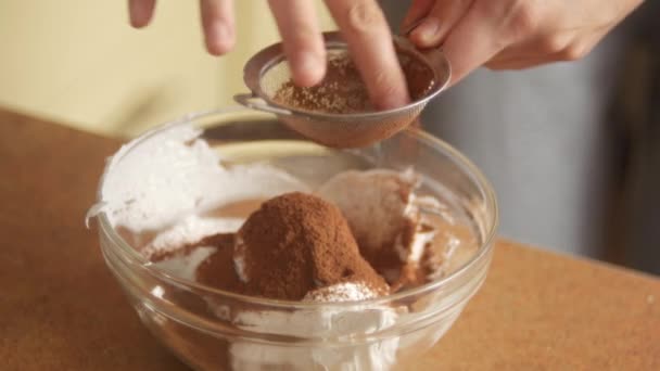 テーブルの上でお菓子を調理し、台所でココアパウダーやチョコレートパウダーとホイップクリームを混ぜます — ストック動画