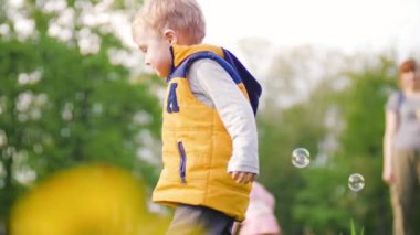 Güneşli bir günde parkta sabun kabarcıklarıyla oynayan küçük sevimli çocuk. Yavaş Çekim 4k