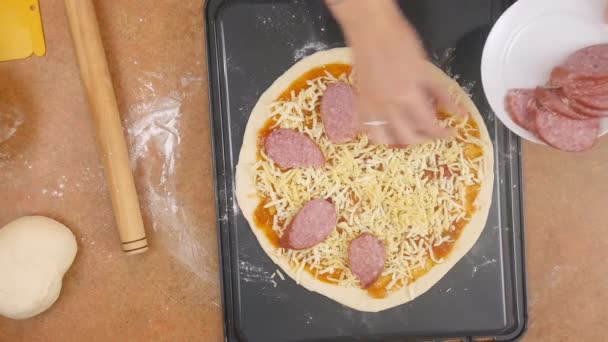 Homem ou mulher chef irreconhecível na pizza coberta por queijo estabelece pedaços de salsicha fatiada para fazer pizza apetecível pepperoni em câmera lenta close up top view 4K vídeo — Vídeo de Stock
