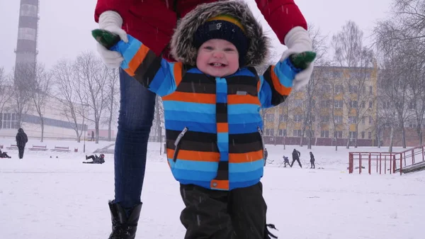 Matka prowadzi dłonie małego uśmiechniętego dziecka w śniegu w parku. Pierwsze kroki dla dziecka. Opieka rodzicielska — Zdjęcie stockowe