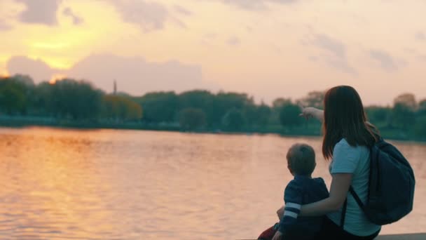 Mor og lille søn sidder på promenaden og ser solnedgangen – Stock-video
