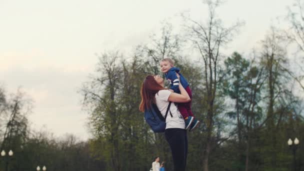 Glückliche und freudige Mutter m kleinen Jungen gehen im Park spazieren. Mutter wirft ihren Sohn nach oben — Stockvideo