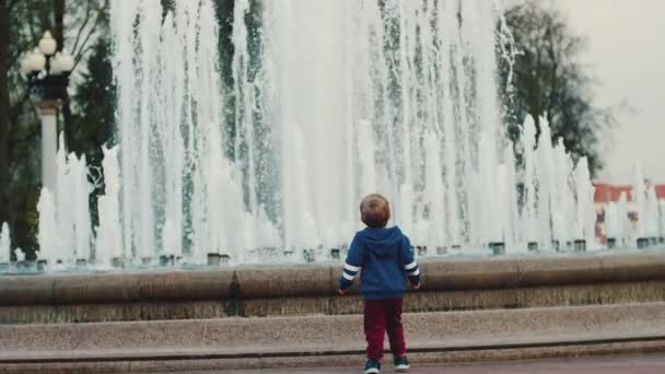 Ein kleiner Junge geht am Brunnen entlang. Gehen Sie mit Ihren Eltern. Elternbetreuung — Stockvideo