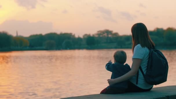 Mamá e hijo se sientan junto al agua y observan el atardecer — Vídeos de Stock