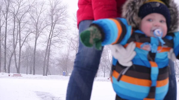 Giovane madre con un bel bambino stanno camminando in un parco invernale con tempo nevoso. Famiglia felice — Foto Stock