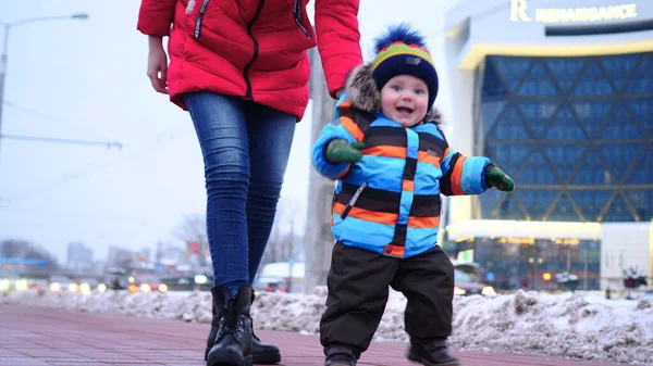 Mamma e bambino camminano per strada in inverno. Un bambino felice sta sorridendo alla telecamera. Rallentatore — Foto Stock