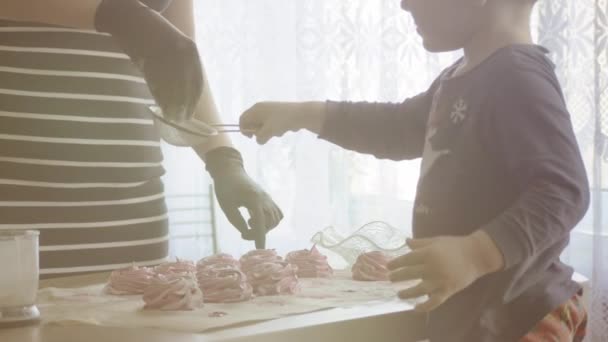 Menino bonito ajuda a mãe a polvilhar marshmallows caseiros com açúcar em pó. Mãe ensina a criança a cozinhar doces caseiros — Vídeo de Stock