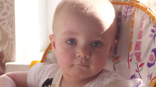 Hermoso niño pequeño sentado en la mesa de los niños, mirando pensativamente a la cámara y alrededor de sí mismo con la ventana de sol en el fondo cerca de la vista frontal video en cámara lenta en 4K — Foto de Stock