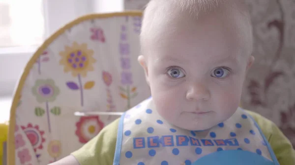 Mooie baby jongen aan de tafel nemen een koekje in zijn hand, eten, kijken in de camera en babbelen close-up bekijken slow mo video in 4K — Stockfoto