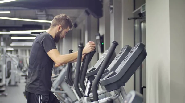 तरुण स्नायू मॅन ट्रेनर एल्लिपॉइड मशीनवर व्यायाम करीत आहे. जिम सुविधा असलेल्या पार्श्वभूमीवर — स्टॉक फोटो, इमेज