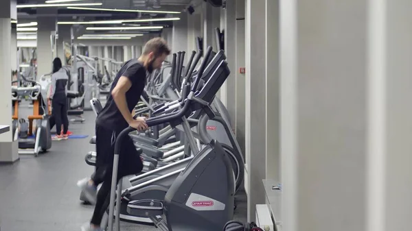 Homem Muscular Jovem Exercício na máquina de simulador de escalada. em segundo plano com uma academia — Fotografia de Stock