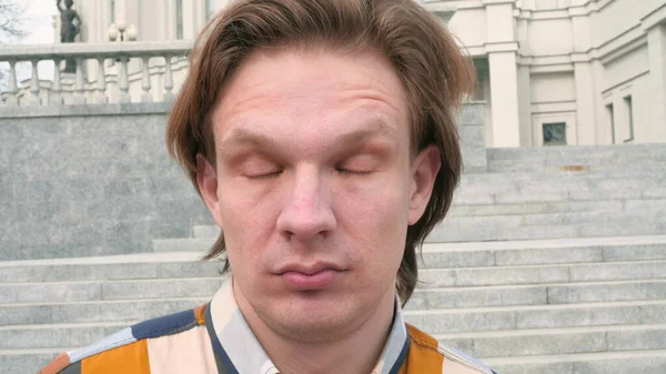 Porträt eines weißen europäischen Mannes, der müde in die Kamera auf Stadtarchitektur blickt, Hintergrund Zeitlupe Nahaufnahme Video in 4K — Stockfoto
