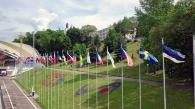 Güneşli bir günde mavi gökyüzüne karşı rüzgarda dalgalanan bayrak direkleri üzerinde farklı ülkelerin bayrakları. 4K