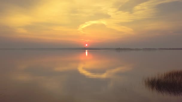 Hermoso amanecer sobre el lago. Reflejo del cielo naranja y del sol en una superficie de agua perfectamente lisa. Disparos con drones. La cámara retrocede — Vídeos de Stock