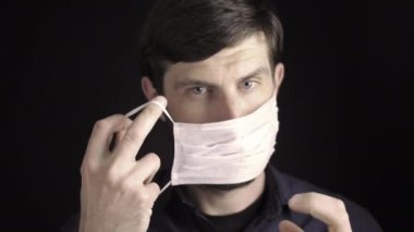 Sakallı beyaz bir adam tek kullanımlık tıbbi bir maske takar, maskeyi düzeltir, iyi niyet gösterisi yapar. Siyah arka plan. Koruma maskeli adamın portresi. Salgın durumu