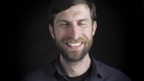 Portrait d'un bel homme barbu. Souriant à la caméra, expression sérieuse du visage. Regarde dans la caméra. Un gars sur fond noir. Mouvement lent — Video