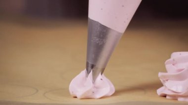 Hamur tüpü mutfaktaki bir yemek tepsisine krema serpiştirdi. Şefin elleri kremalı pasta pişiriyor. Yakın çekim.