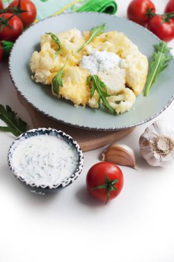 Beyaz arka planda krem-sarımsak soslu fırında karnabahar ve domates.