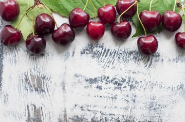 Beyaz ahşap arka planda yeşil yapraklı tatlı kirazlar. Üst görünüm