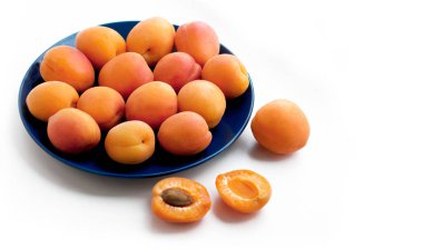 Beyaz zemin üzerinde mavi tabakta olgun kayısılar