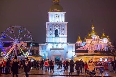 Kiev, Ukrayna - 3 Ocak 2018: İnsanlar Noel pazarı ve dönme dolap Saint Michael Altın Kubbeli Manastırı saat kulesi önünde ziyaret edin. Seçici odak
