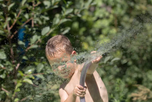 Menino esguichando água de uma mangueira — Fotografia de Stock
