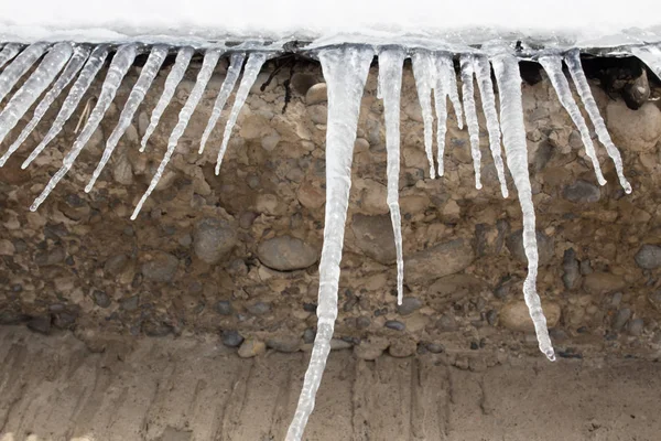 Large icicles hanging on the roof of the house in springtime — Stock Photo, Image