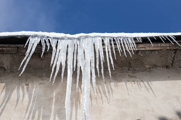 Large icicles hanging on the roof of the house in springtime