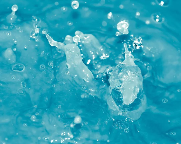 Droppar vatten som faller i blått vatten — Stockfoto