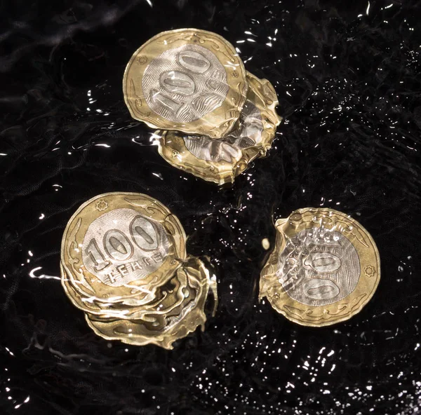 Coins in water splashes on a black background — Stock Photo, Image
