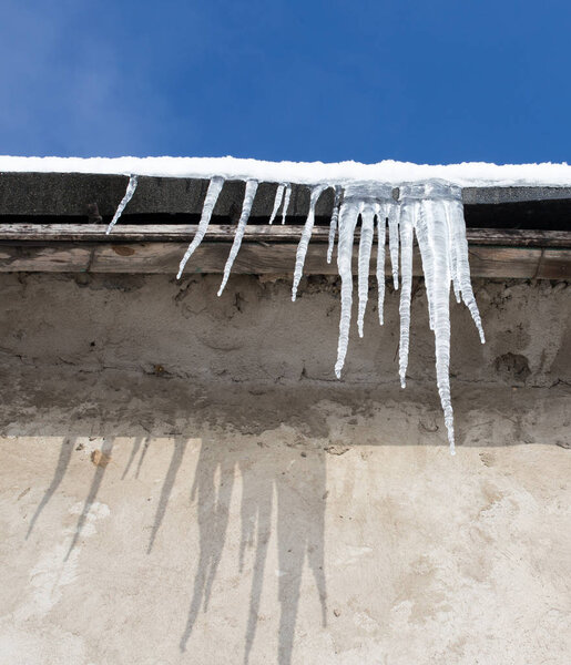 Large icicles hanging on the roof of the house in springtime
