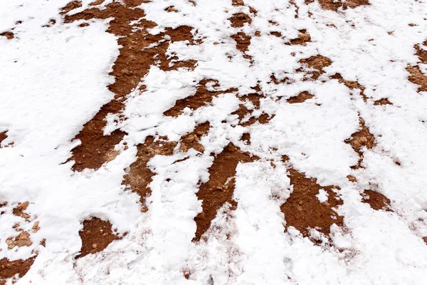 Snö på röd lera i naturen — Stockfoto