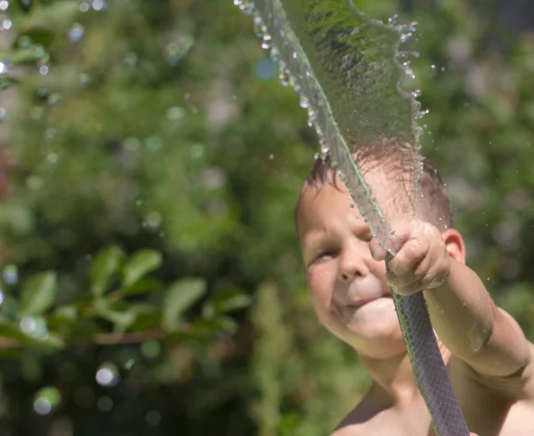Menino esguichando água de uma mangueira — Fotografia de Stock