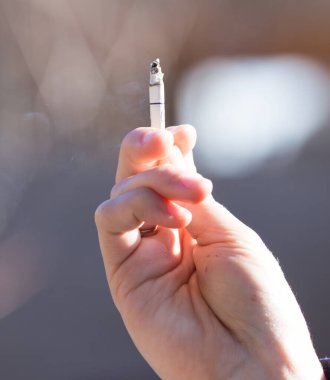 Bir kadının elinde sigara var. Doğadaki parkta.