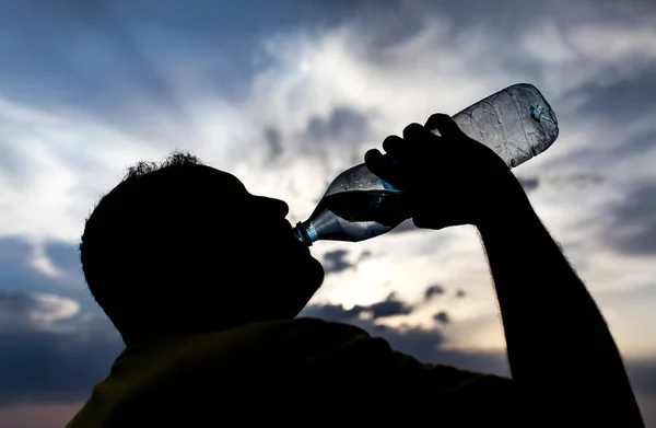 日落时喝水的男人的轮廓 — 图库照片