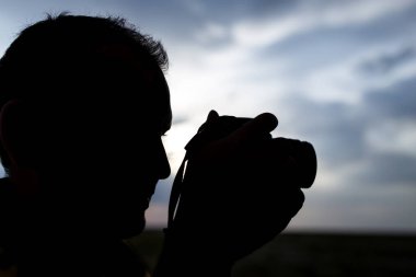 Günbatımı arka planında kamera olan bir adamın silueti. .