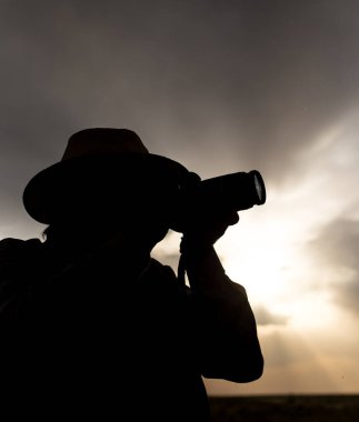 Günbatımı arka planında kamera olan bir adamın silueti. .