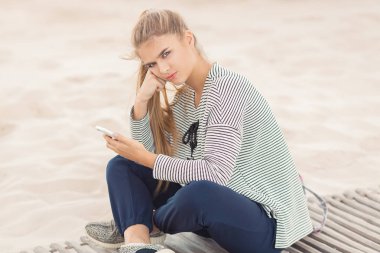 Kumsalda akıllı telefonu olan bir kadın. Tatil ve teknoloji.