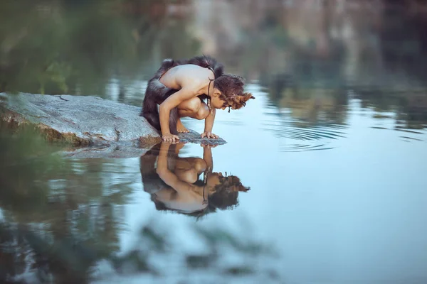 Barlanglakó ősember. Kisfiú ül a strandon és úgy néz ki, a víz — Stock Fotó