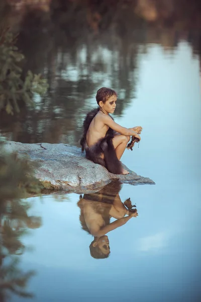 Homme des cavernes. Petit garçon assis sur la plage et regarde l'eau — Photo