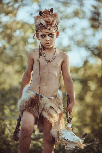 Angry caveman, manly boy with stone axe and animal skull. Prehistoric tribal boy outdoors on nature. Young shaggy and dirty savage, warrior and hunter with weapon. Primitive ice age man in animal skin — Stock Image Angry Caveman Manly Boy Stone Axe Animal Skull Prehistoric Tribal Royalty Free Stock Images