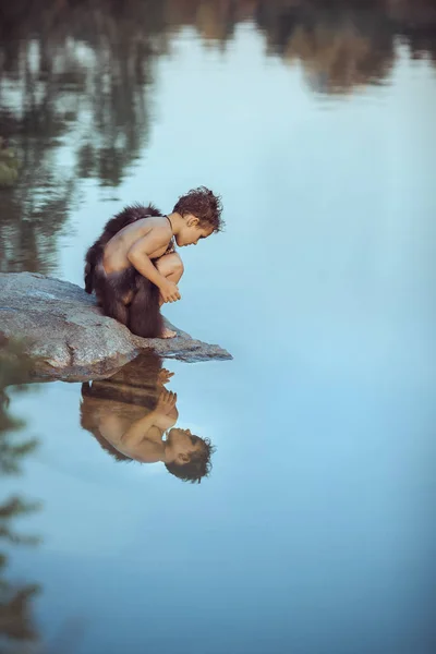 Caveman. Little boy sitting on the beach and looks at the water — Stock Image Caveman. Little boy sitting on the beach and looks at the water Royalty Free Stock Photos