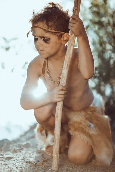 Cute caveman, manly boy with staff hunting outdoors. Ancient warrior